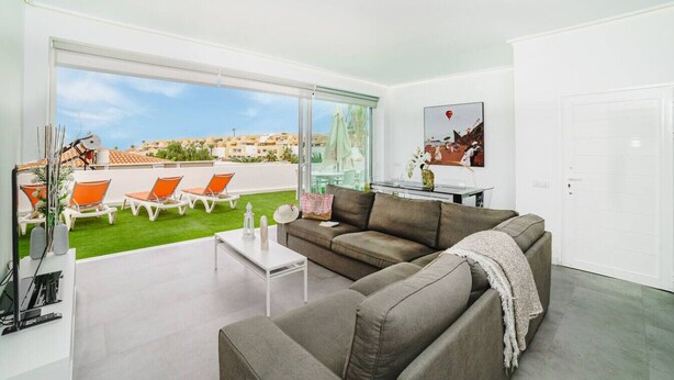 A modern living room with a grey sofa, a small white table, and orange lounge chairs on a balcony with a city view. - Villa Carlota (Costa Adeje) (Costa Adeje)