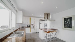 A modern kitchen with a granite countertop, stainless steel appliances, and a bar area with stools. - Villa Carlota (Costa Adeje) (Costa Adeje)