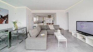 A modern living room with a grey sectional sofa, a glass dining table, and a flat-screen TV. - Villa Carlota (Costa Adeje) (Costa Adeje)