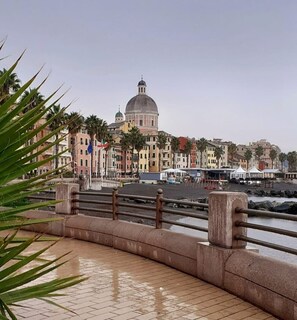 A waterfront promenade with a domed building in the background, palm trees, and a tiled walkway. - Andreas Haus, your safe haven for beach vacations or visits to Genoa (Genova)