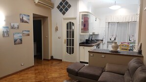 A living room with a brown sofa, a kitchen with white cabinets, and a dining area with a table and chairs.