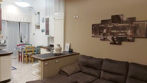 A living room with a brown sofa, a dining area with a table and chairs, and a kitchen area with cabinets and a sink.
