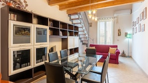 A spacious living area with a glass-top dining table, black chairs, a red sofa, and a staircase with a metal railing.