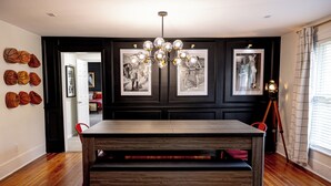 A dining area with a wooden table, chairs, and a chandelier. There are framed pictures on the wall and a basketball hoop decoration. - NEW Luxe Retro Sports Retreat~Walk to Stadiums (Raleigh)