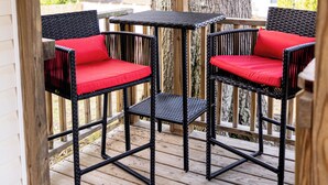 A wooden deck with two wicker chairs and a small table, surrounded by a wooden railing and a large tree. - NEW Luxe Retro Sports Retreat~Walk to Stadiums (Raleigh)