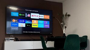 A modern living room with a flat-screen TV mounted on the wall displaying various app icons.