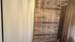 A bedroom with a wooden wall, a white wardrobe, a fluffy pillow, and a hanging light fixture.