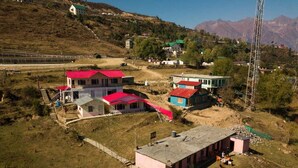 A rural area with several buildings, including a house with a red roof and a small structure with a pink roof. - The Snow City Auli (Auli)