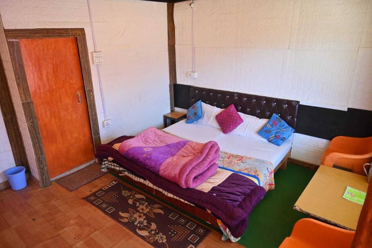 A single bed with a headboard, a wooden door, a small table, and a chair.