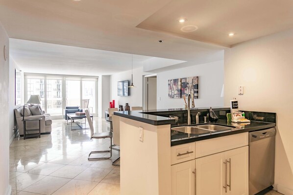A modern kitchen with a central island, a dining area with a sofa and chairs, and a view through a glass door to an outdoor balcony.