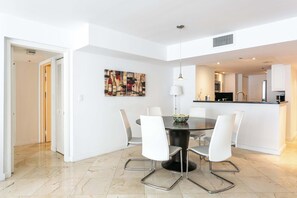 A modern dining area with a round table, white chairs, a pendant light, and a painting on the wall.