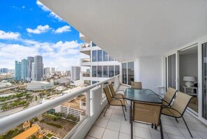A balcony with a glass table and chairs, overlooking a cityscape with modern buildings.