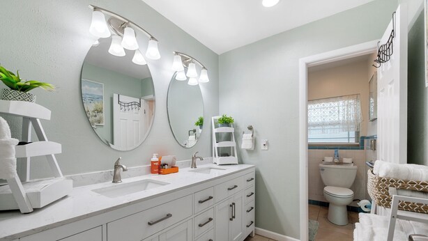 A bathroom with a white vanity, two sinks, a large mirror, and a toilet.