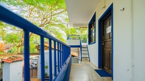 A corridor with a blue railing, a door with a sign, and a view of a parked vehicle and greenery outside. - Casa German Near The Beach (Calangute)