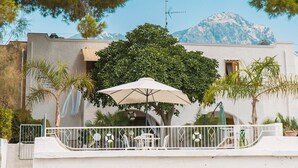 A white building with a balcony, a large umbrella, and a mountain in the background. - Luxury Villa on the Beach in Diamante, Sea View - Villa Ventre (Belvedere Marittimo)