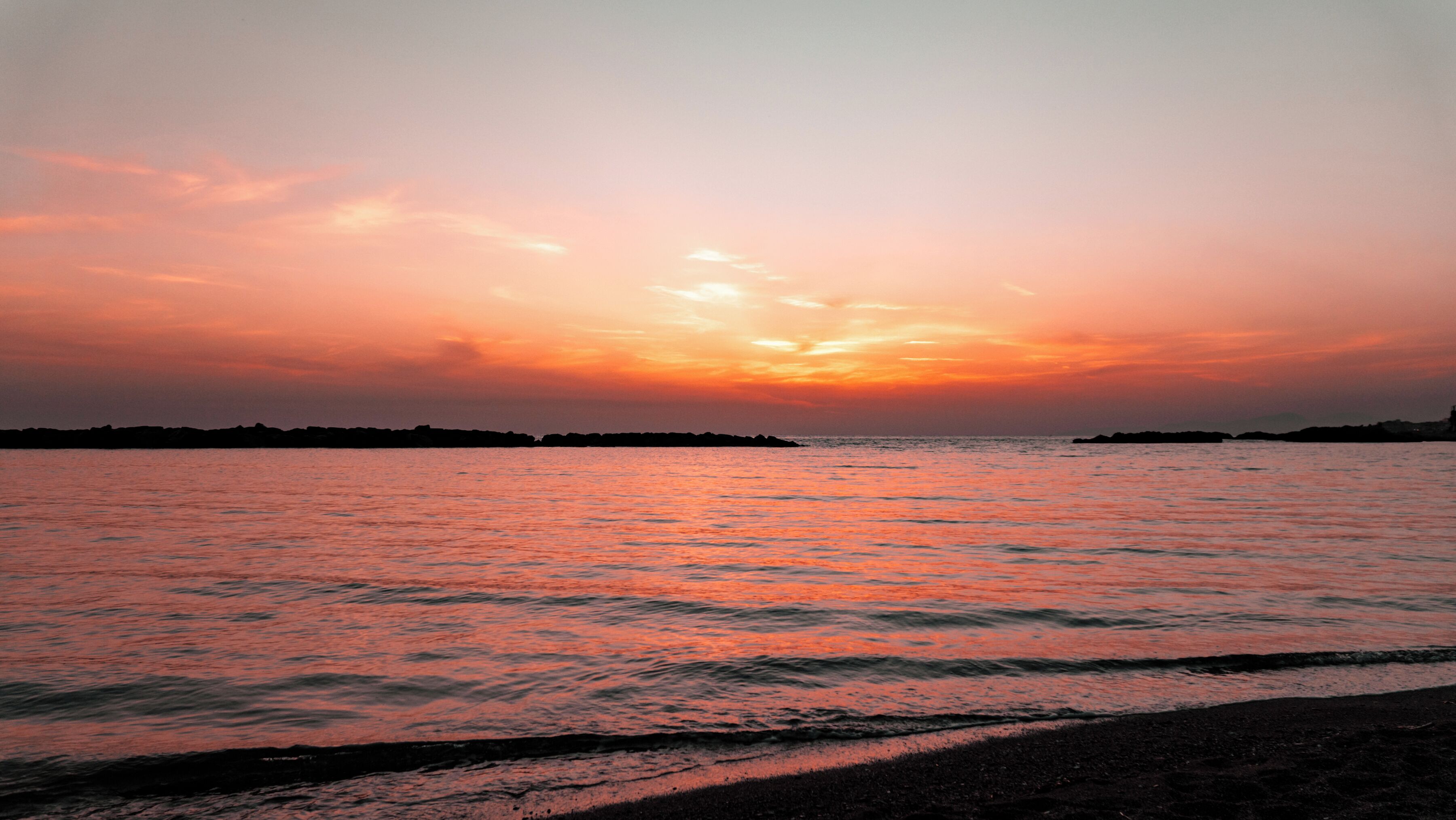A sunset over a calm sea with a distant shoreline silhouette.