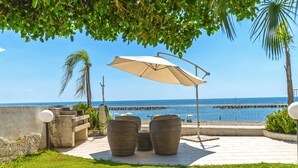 An outdoor patio with a view of the sea, featuring a table and chairs under a canopy, a stone wall, and a palm tree. - Luxury Villa on the Beach in Diamante, Sea View - Villa Ventre (Belvedere Marittimo)