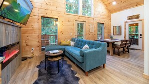 A cozy cabin interior with a sectional sofa, a dining table, and a TV mounted on the wall. - Couples Private Mountain Oasis!! Hot Tub! Theatre! Fire Pit! (Sevierville)