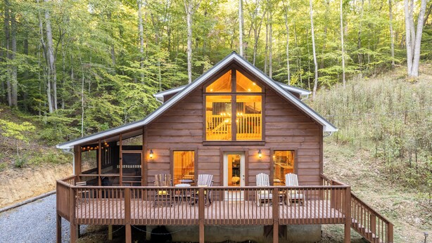 A wooden cabin with a deck, a porch, and a staircase leading to the entrance. - Couples Private Mountain Oasis!! Hot Tub! Theatre! Fire Pit! (Sevierville)