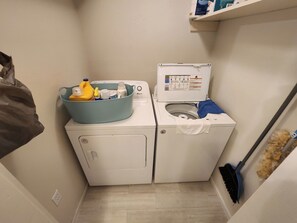 A compact laundry area with a washing machine and dryer, a blue laundry basket on the washer, and a broom leaning against the wall. - Lake Views, Water Trail and Minutes to the Marina (Higden)