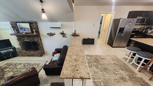 A spacious living room with a fireplace, a kitchen area with a refrigerator, and a dining area with bar stools. - Rock Ledge at the Narrows (Higden)