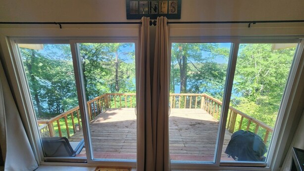 A room with large windows overlooking a wooden deck and a forested area. - Rock Ledge at the Narrows (Higden)