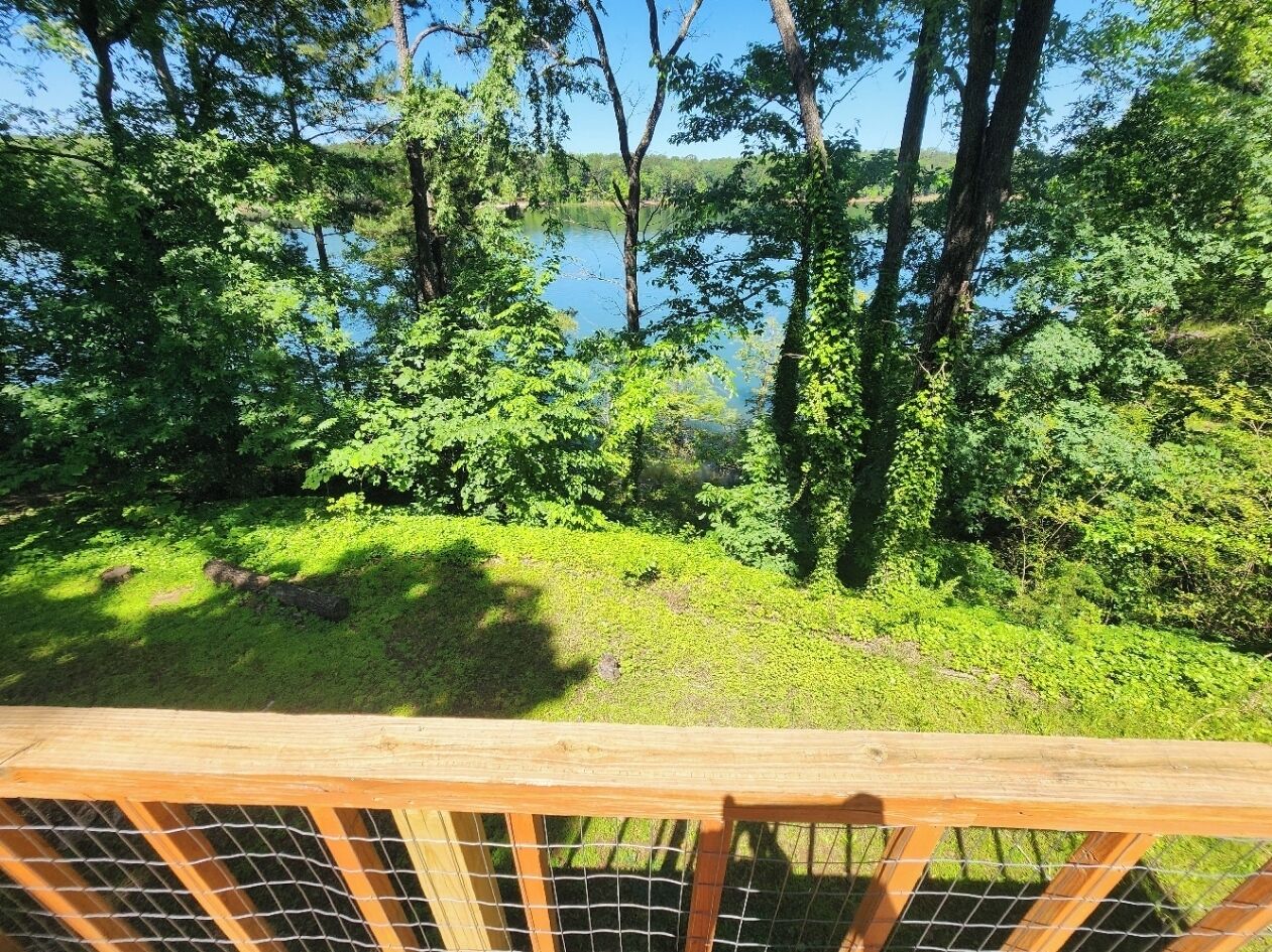 A wooden deck overlooking a lake surrounded by dense green foliage.