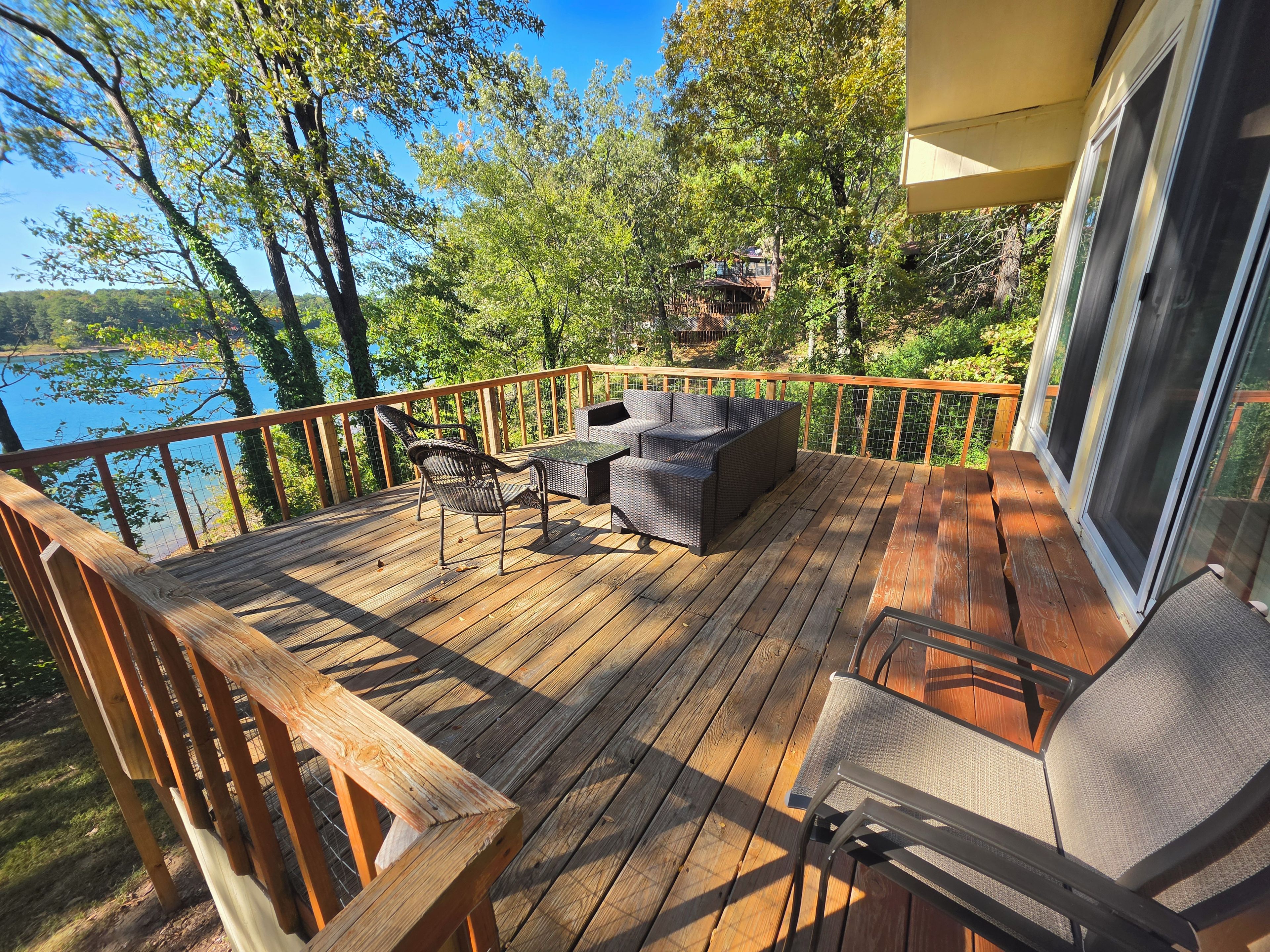 Une terrasse en bois, agréée de mobilier d’extérieur, qui offre une vue sur une étendue d’eau et est entourée d’arbres.