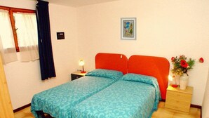 Un lit double recouvert d’une couvre-lit bleue à motifs, une table de chevet avec une lampe, un tableau encadré accroché au mur et un vase rempli de fleurs posé sur la table de chevet.