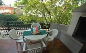 A balcony with a table set for two, surrounded by white chairs. - Comfortable Three Room Apartment in Lignano With Parking (Lignano Sabbiadoro)