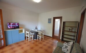 A compact living space with a dining area, a television, a sofa, and a bookshelf. - Comfortable Three Room Apartment in Lignano With Parking (Lignano Sabbiadoro)