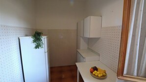 Une petite cuisine avec un réfrigérateur blanc, un meuble de rangement blanc et un panier de fruits posé sur le plan de travail.