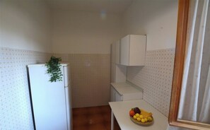 Une petite cuisine avec un réfrigérateur blanc, un meuble de rangement blanc et un panier de fruits posé sur le plan de travail.