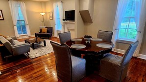 Amplia sala de estar con piso de madera, una mesa de comedor con sillas, un sofá y un televisor montado en la pared.