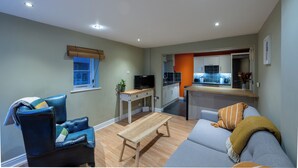 Een moderne woonkamer met een bank, een fauteuil, een houten salontafel en een televisie op een meubel.