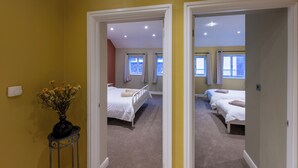Een slaapkamer met twee bedden, een bloemenvaas en een uitzicht op een andere kamer door een geopende deur.