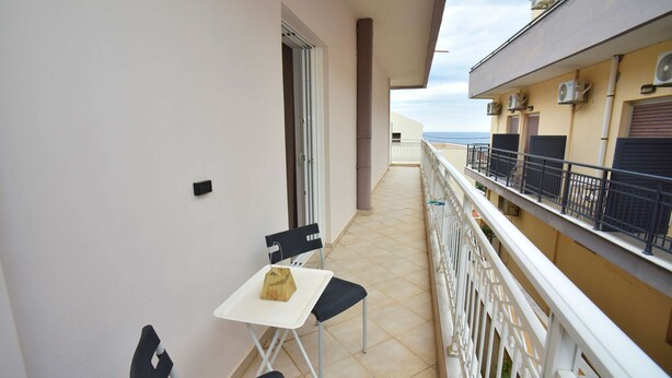 Een balkon met een tafel en stoelen, airconditioners en uitzicht op zee.