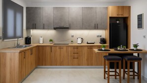 A modern kitchen with wooden cabinets, a black refrigerator, and a bar area with stools. - Lavish Living Suite Heraklion Crete (Hersonissos)