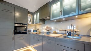 A modern kitchen with grey cabinetry, a built-in oven, a microwave, and a sink with a unique faucet design.