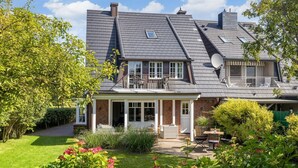 A two-story house with a covered porch, a satellite dish, and a garden with flowers and shrubs.
