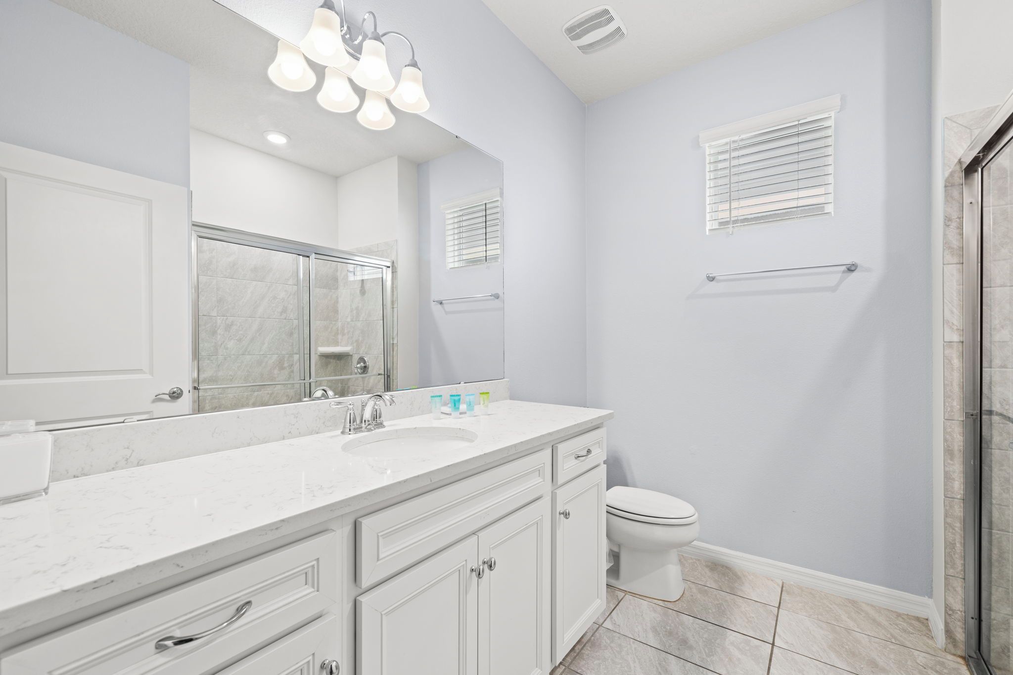 A modern bathroom with a large mirror, a shower enclosure, a toilet, and a vanity with drawers and a sink.