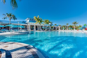 A large outdoor swimming pool with lounge chairs and umbrellas, surrounded by palm trees and modern buildings. - 2210 Lelani Circle (Davenport)