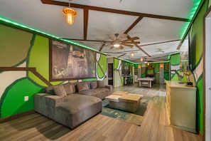Ein Zimmer mit einer Couch, einem Billardtisch und einem Wandgemälde im Grünton.