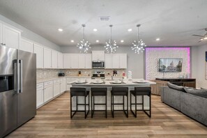 A modern kitchen with a central island, stainless steel appliances, and a seating area with a gray sofa. - 2210 Lelani Circle (Davenport)