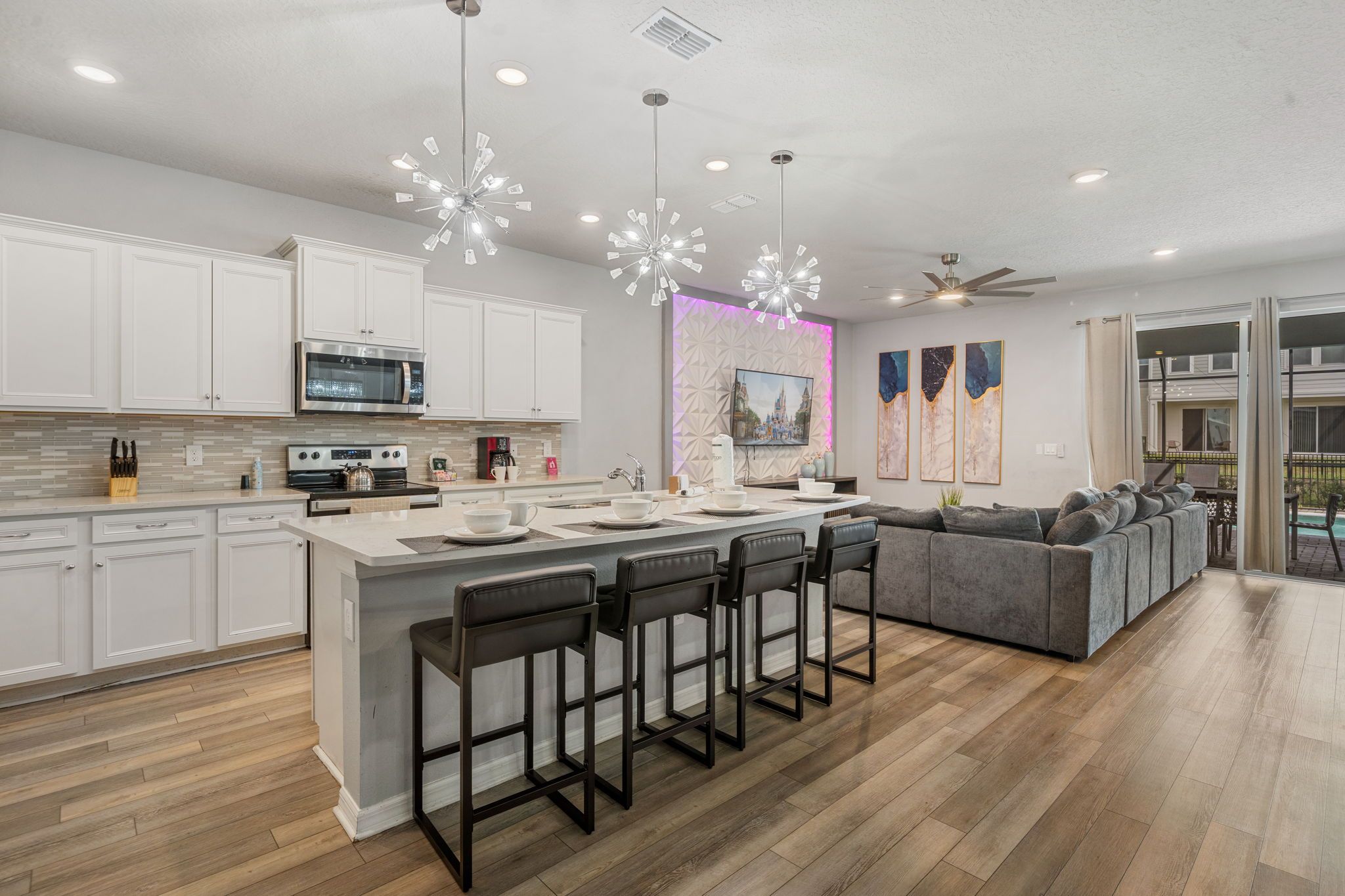 A modern kitchen with white cabinets, a central island with bar stools, a microwave, and a large window.
