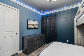 A bedroom with a bed, a dresser, a wall-mounted TV, and a window with curtains. - 2210 Lelani Circle (Davenport)