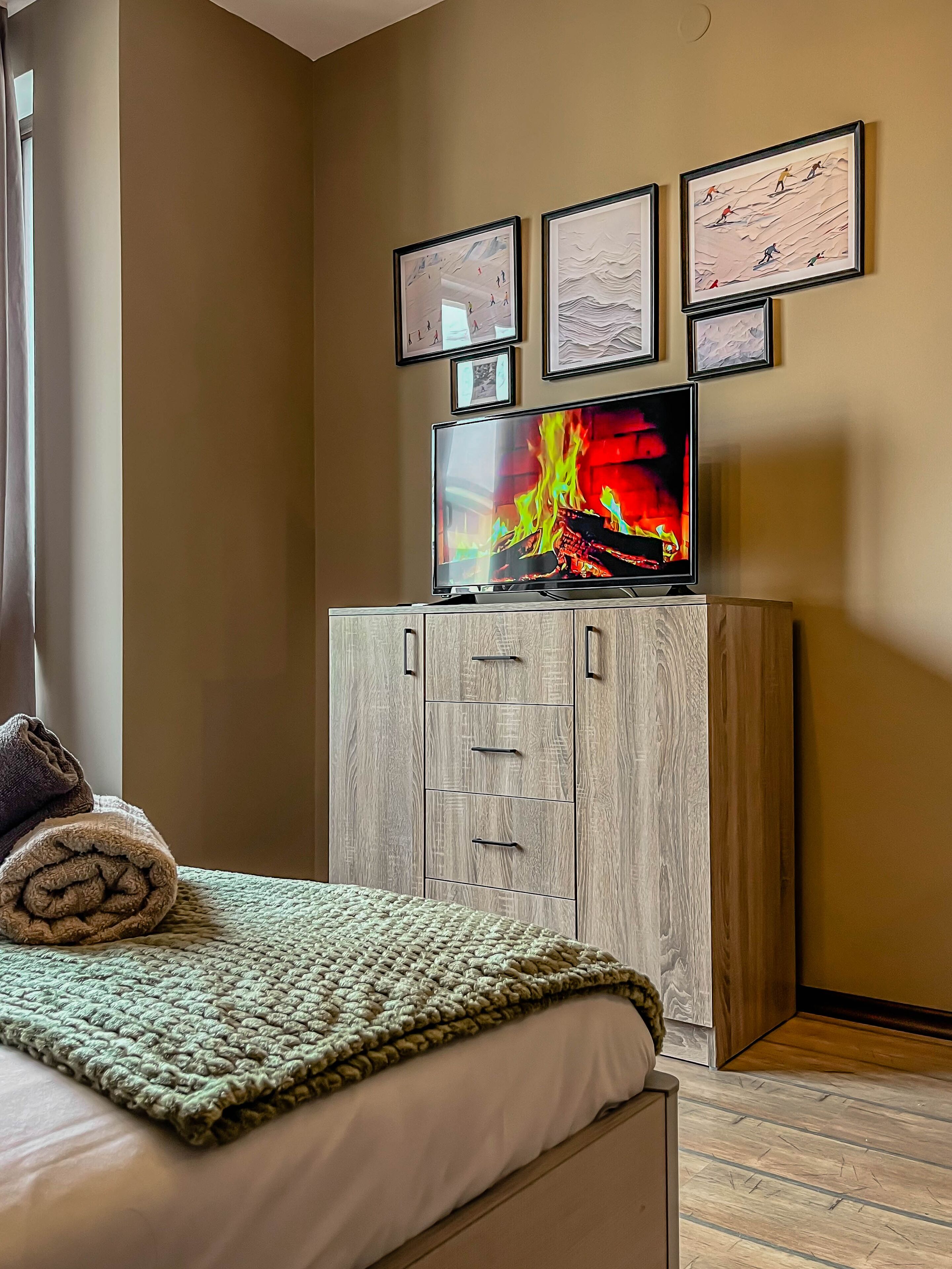 A bedroom with a bed, a television on a wooden cabinet, and framed artwork on the wall.