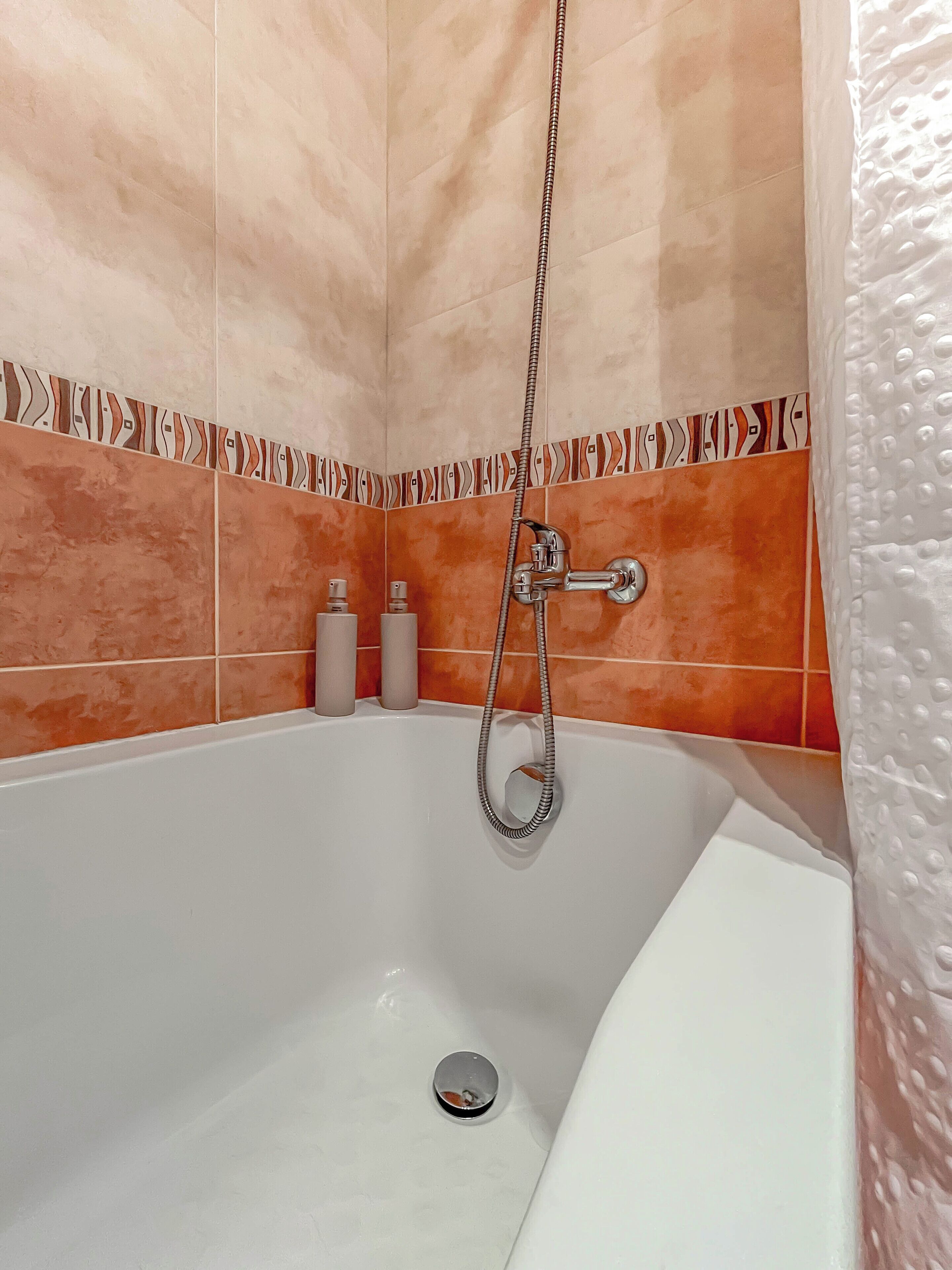 Un baño con una bañera blanca, paredes de azulejos anaranjados y un cabezal de ducha.