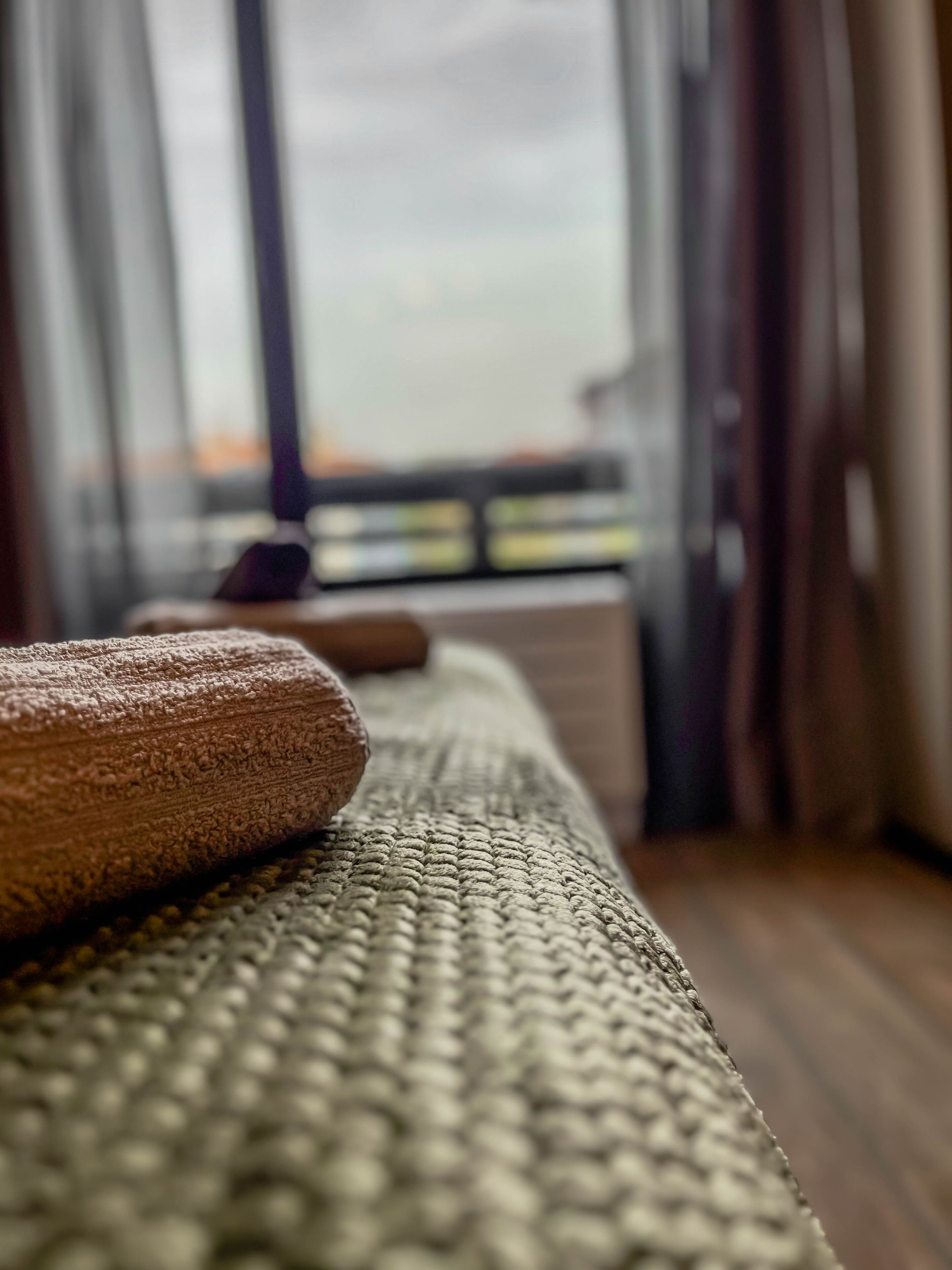 A massage table with towels and a massage stone, set against a window with curtains.