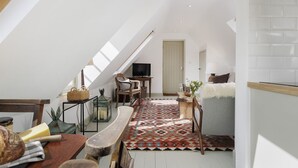Habitación estilo loft con techo inclinado, una mesa de comedor de madera, un televisor, un tapete estampado y una zona de estar acogedora con una silla y cojines.